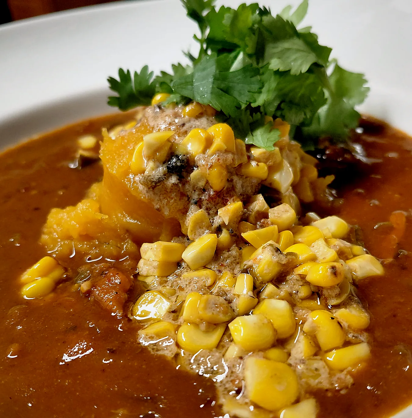 A bowl of squash soup topped with sweet corn and fresh cilantro